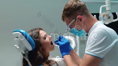 年轻的牙医戴着医用手套，戴着口罩，检查年轻的黑发女子`病人使用牙科器械的牙齿问题